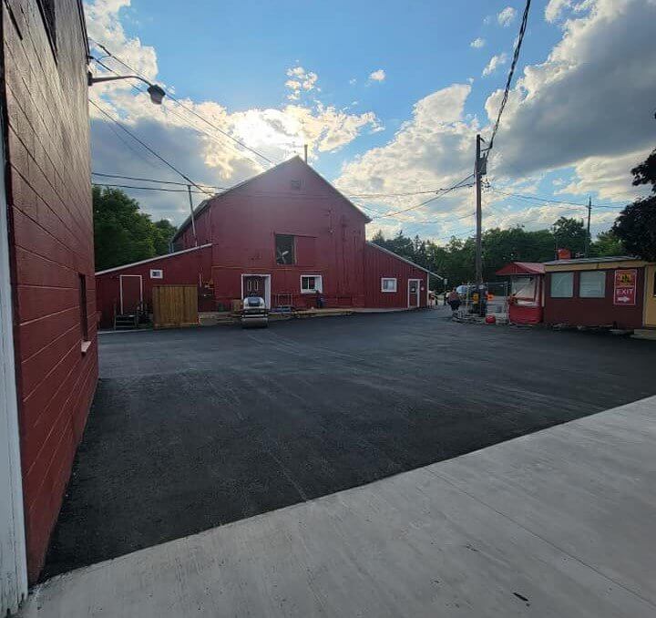 A large red barn in Hamilton with a paved driveway that King Asphalt just finished paving. The barn has a steep roof and a utility pole beside it. There is a small red structure with signage to the right.